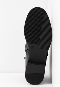 Suela de zapato negra con textura acanalada, mostrando un diseño plano y forma redondeada. Talla 37 marcada en un lado. Estilo minimalista.