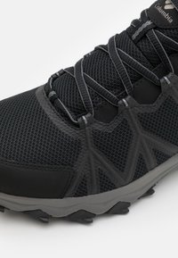 Czarne buty sportowe z siateczkową cholewką, szarym gumowym podejściem z ząbkowanym bieżnikiem oraz elastycznymi sznurowadłami zapewniającymi stabilne dopasowanie. Z wyróżniającym się logo.