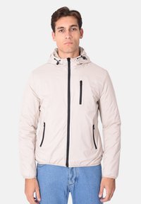 Giacca in nylon beige chiaro con cappuccio, zip nera e due tasche laterali. Tessuto liscio con lacci regolabili sul cappuccio.