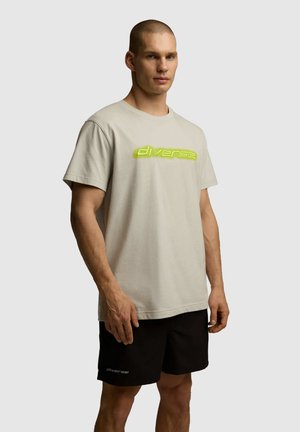 Jasnobeżowa bawełniana koszulka z odważnym, odblaskowym zielonym logo, w połączeniu z czarnymi szortami z podobnym detalem logo.