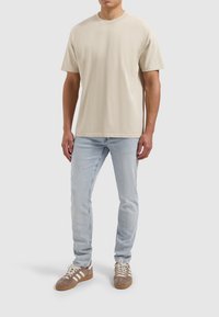 Beige katoenen T-shirt met ronde hals, gecombineerd met lichtblauwe spijkerbroek. Schoeisel is bruin suède met witte en beige strepen.