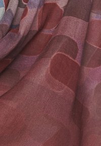 Tissu transparent avec une surface texturée dans des rouges profonds et des violets, présentant des motifs circulaires abstraits disposés en couches.