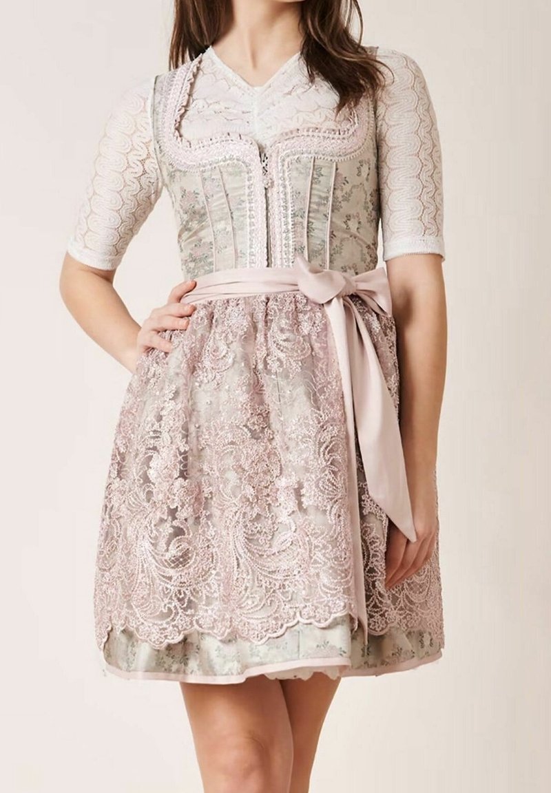 Vrouw in een lichtroze en grijs gebloemd dirndl-jurkje met een kanten schort, geplooide halve mouwen en een strik in de taille.