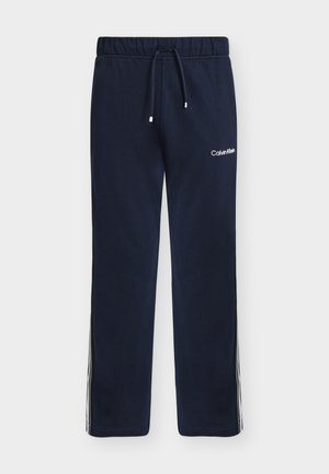 Navy blue sweatpants with elastic waistband, drawstring, Calvin Klein logo on thigh, and white side stripes.
