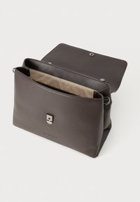 Braune Lederhandtasche mit glatter Textur, einem magnetischen Klappenverschluss und einem gefütterten Innenraum mit Fischgrätmuster.