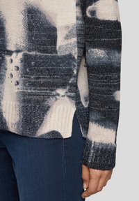 Pullover mit einer Kombination aus cremefarbenen und dunkelblauen Tönen, strukturiertem Strick, geripptem Saum und seitlichen Schlitzen. Metallische Akzente verleihen dezenten Glanz.