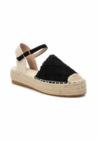 Espadrille de tejido negro con una suela de plataforma de yute natural, tiras en el tobillo de color beige y una puntera redonda con un acento trenzado.