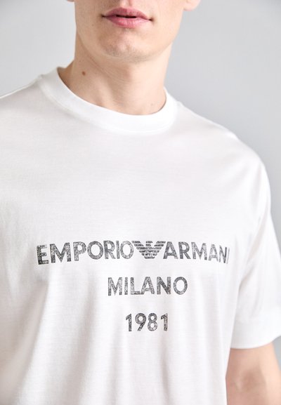 T-shirt en coton blanc avec le texte imprimé en noir "EMPORIO ARMANI MILANO 1981" et logo, design col rond et manches courtes.