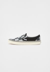 Zapato slip-on a cuadros en negro y gris con parte superior de lona, acentos negros contrastantes y suela de goma blanca con etiqueta de logo.