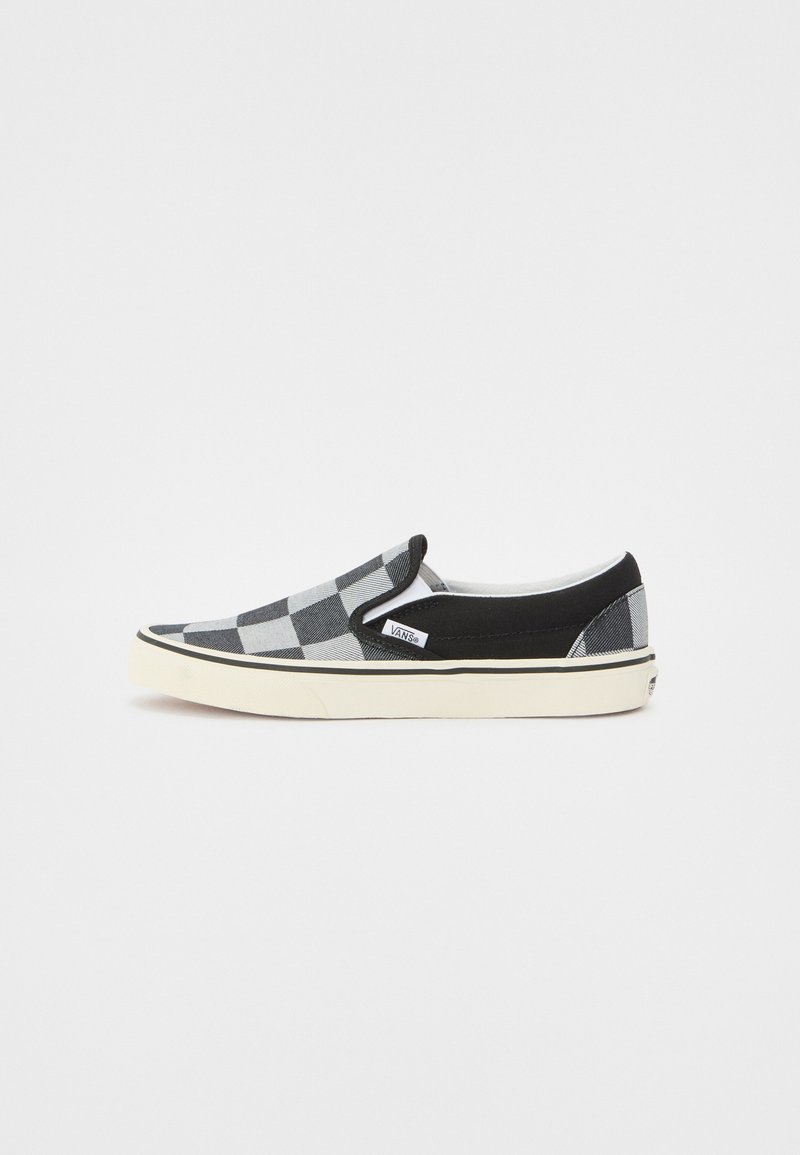 Zapato slip-on a cuadros en negro y gris con parte superior de lona, acentos negros contrastantes y suela de goma blanca con etiqueta de logo.