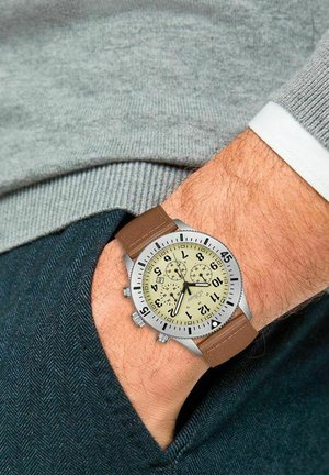 Bruin lederen armbandhorloge met een zilveren roestvrijstalen kast, crèmewitte wijzerplaat, zwarte Arabische cijfers en drie sub-dials voor chronografische functies.