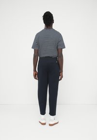 Ριγέ πουκάμισο με κοντά μανίκια σε ναυτικό μπλε και άσπρο; συνδυασμένο με στενά παντελόνια σε ναυτικό μπλε; λευκά αθλητικά παπούτσια; ορατές πίσω τσέπες; λεία υφή.