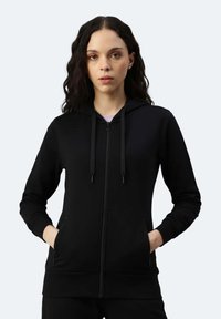 Felpa nera con zip, cappuccio regolabile con coulisse, tasche frontali, polsini e orlo a coste. Tessuto morbido dalla trama liscia.