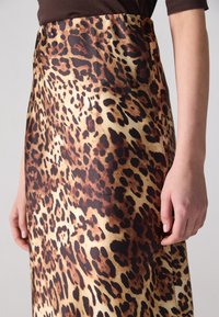 Suknja s leopard uzorkom u nijansama smeđe i bež. Glatka tekstura s uskim strukom i detaljima na bočnim šavovima. Kratki kadar ruke na rubu.