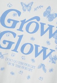 Biała bawełniana koszulka z jasnoniebieskim nadrukiem. Posiada duży napis "Grow Glow" oraz ilustracje kwiatów i motyli.