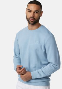 Sudadera azul claro en mezcla de algodón, con cuello redondo, manga larga y un sutil logo en el pecho. Textura suave, corte regular.