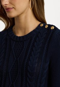 Maglione lavorato a maglia blu navy con un design a cavo testurizzato, scollatura rotonda e bottoni decorativi dorati sulla spalla.