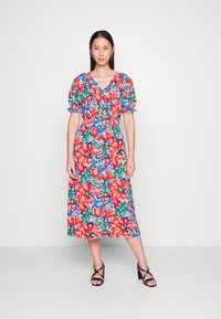 Vestido midi floral com mangas bufantes, apresentando um decote em V. As cores incluem vermelho, azul, verde e branco. Tecido leve e solto.
