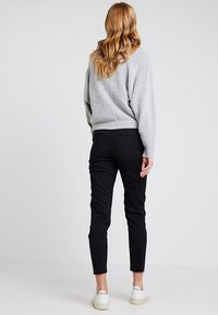 Grå stickad tröja, svarta tajta byxor och vita sneakers. Tröjan har en ribbad fåll och vida ärmar, vilket visar en mjuk textur.