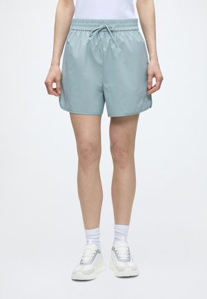 Personne portant un short bleu clair à cordon, des chaussettes blanches et des baskets blanches, debout devant un fond blanc uni.