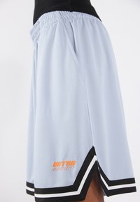 Gaiši zili sieta basketbola šorti, kuros ir melna josta, baltas sānu svītras un oranžs zīmola logotips apakšā.