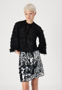 Μαύρη, υφασμένη μπλούζα με ξεθωριασμένες λεπτομέρειες, συνδυασμένη με μια ασημένια φούστα μίνι με παγιέτες. Φαρδιές μανσέτες και εφαρμοστό φορεμά.