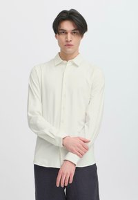 Light cream long-sleeve shirt made of a soft fabric; features a collar and button-down front, paired with dark pants.