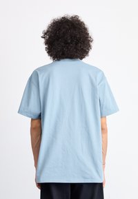 Light blue cotton t-shirt with short sleeves and a crew neckline, featuring a relaxed fit and minimal stitching details on the back.