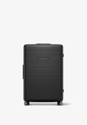 Valise rigide noire avec un design rainuré, une poignée supérieure, deux roues latérales et un panneau avant plat. Dispose d'un emplacement pour une étiquette de bagage au-dessus de la poignée.