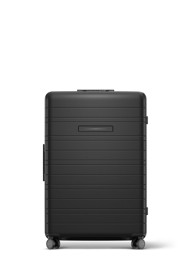 Black hard-shell suitcase with ridged design, top handle, two side wheels, and a flat front panel. Features a luggage tag slot above the handle.