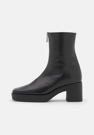 Bottine noire en cuir lisse avec un bout arrondi et un talon épais texturé. Dispose d'une fermeture éclair latérale.