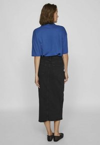Blue short-sleeve top paired with a black denim midi skirt. Skirt features back pockets and a fitted silhouette. Black flat shoes.