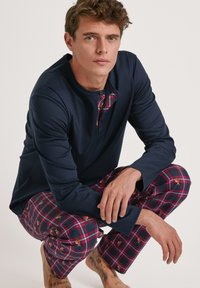 Marineblauw shirt met lange mouwen met een geruit accent bij de kraag; bijpassende geruite pyjamabroek in rood en marineblauw met kreeftmotieven.