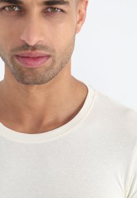 Világos krém színű póló klasszikus kerek nyakkivágással, puha, texturált anyagból készült, és karcsú szabású.