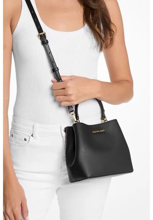 Bolso de mano de cuero negro con un asa corta y una correa de hombro desmontable. Cuenta con una placa de logotipo dorada, textura suave y diseño minimalista.