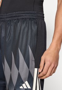 Μαύρο αθλητικό σορτς με υφή και γκρι ζιγκ ζαγκ μοτίβα, ελαστική μέση με κορδόνι και αντανακλαστικές λευκές λεπτομέρειες.