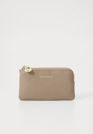 Tan leather zip wallet with textured surface, gold hardware, and embossed logo on the front. Compact rectangular shape.