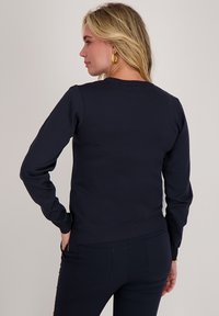 Marineblauwe sweatshirt met lange mouwen, boordjes aan de mouwen en tailleband. Heeft een eenvoudig ontwerp met een ronde hals en een soepele textuur.