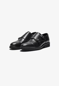 Zwarte leren schoenen hebben twee verstelbare gespen, een ronde neus, een gladde textuur en een lage hak. Klassiek ontwerp met minimalistische details.