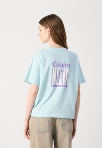 Lichtblauwe katoenen T-shirt met korte mouwen en een ronde hals. Kenmerkt zich door het "Calvin KLEIN"-logo in paars en wit op de achterkant.