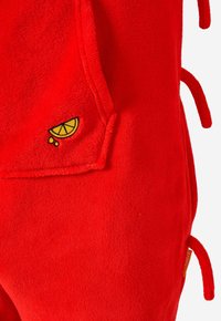 Tela roja brillante con un pequeño diseño bordado de una rodaja de limón amarilla y naranja y lágrima cerca de una costura en la esquina.