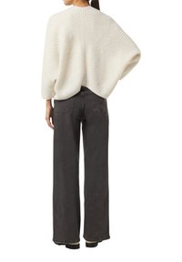 Przesadnie duży kremowy sweter z dzianiny o prążkowanej strukturze i detalami w splocie kablowym, połączony z wysokim stanem ciemnoszarych spodni typu wide-leg.