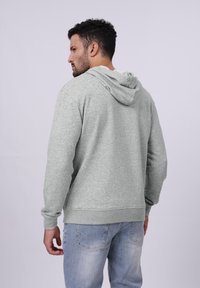 Sudadera con capucha gris de acabado texturizado, que presenta mangas largas, puños acanalados y una capucha con cordón. Se lleva con jeans de color azul claro.