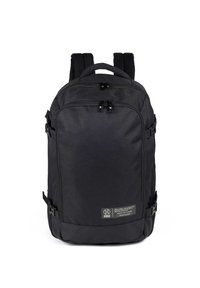 Mochila de tela negra con cremalleras dobles en la parte superior, correas laterales, parte posterior acolchada y una etiqueta de logotipo en el frente. Presenta un diseño rectangular y elegante.