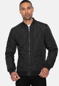 Zwarte quilted bomberjack met een ritssluiting aan de voorkant, ribgebreide manchetten en zoom. Voorzien van zijzakken en een gladde textuur.