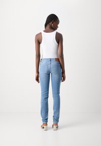 Jeans azzurri in denim, con una vestibilità slim e tasche posteriori. Abbinati a una canotta bianca a costine, mostrati da dietro.