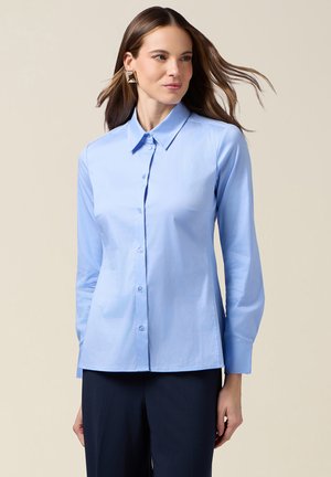 Jasnoniebieska koszula zapinana na guziki z kołnierzykiem, długimi rękawami i gładką fakturą, zestawiona z ciemnogranatowymi spodniami. Prosty, klasyczny krój.