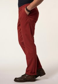 Chino in cotone rosso con design a gamba dritta, due tasche anteriori, chiusura con bottone e orli risvoltati, abbinati a stivaletti in pelle marrone.