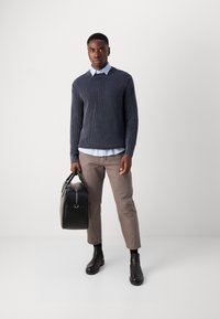 Marine ribbestrikket genser, lyseblå skjorte med krage, beige bukser, svarte lær støvler og en svart veske med rund form og to håndtak.