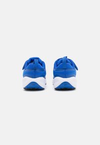 Une paire de chaussures de sport bleues avec des semelles blanches montrées de l'arrière sur un fond blanc uni.